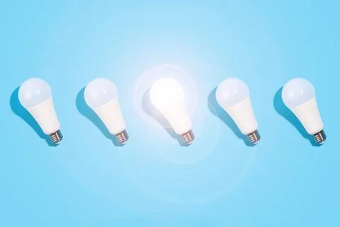 One bright LED light bulb stands out from the rest on a blue background Stock Photos