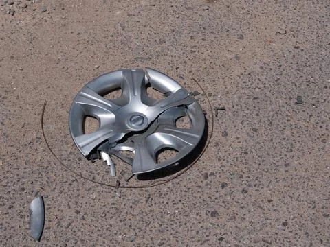 One broken gray dirty plastic car wheel cover lies on the asphalt of the road. Stock Photos