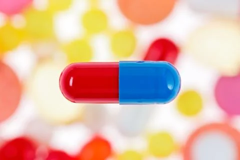 One capsule (pill) macro view on blurred multicolored drugs background, medic Fotos Stock