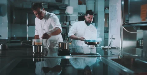 One chef adds a liquid to pot while other stirs pan Stock Footage 204972647