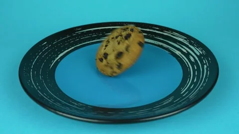 One chocolate chip cookie spinning in a plate. Blue plate on blue background Stock Footage 254976519
