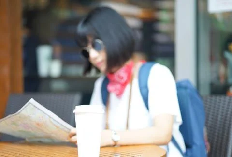 One coffee cups on table with Young traveller woman in background at cafe. Cu Stock Photos