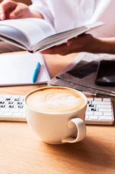 One cup of coffee on a working table and book in a person's hand. Stock Photos
