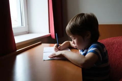 One cute kid is sitting at the table and doing homework. The child writes d.. Stock Photos