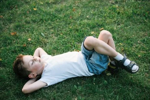 One cute small boy lying on the green grass among fallen leaves in park 스톡 사진