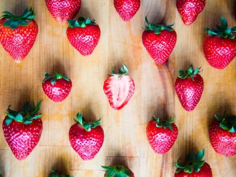 One cutted strawberry in an srranged pattern of strawberries on a wooden boar Stock Photos