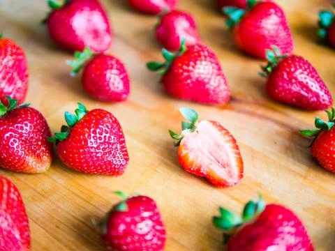 One cutted strawberry in an srranged pattern of strawberries on a wooden boar Stock Photos