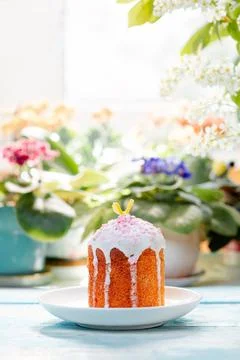One decorated Easter bread on a plate. In the background-plants and flowers.  Stock Photos