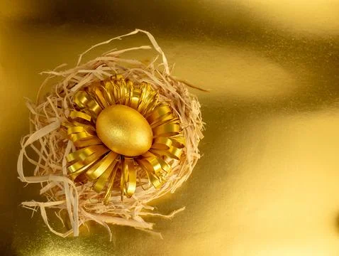 One Easter egg, painted gold and black, lies in a nest on a glittering gold.. Стоковые фото
