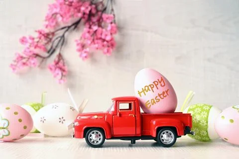 One Easter egg on a small car on a light background and blooming branch. Stock Photos