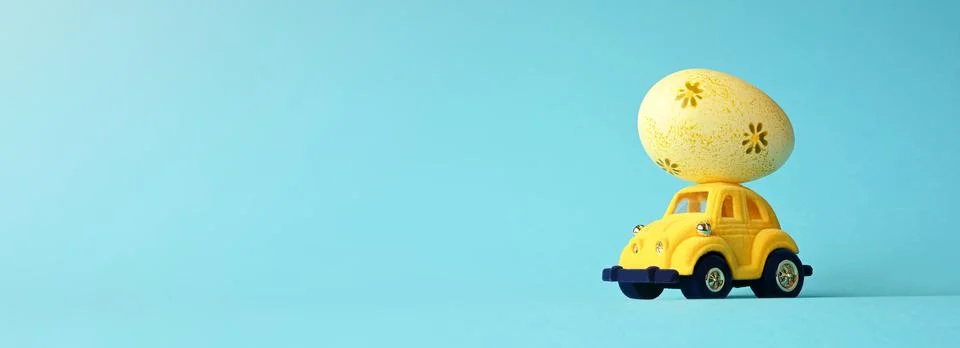 One Easter egg on a small car on a blue background. Copy space. Stock Photos