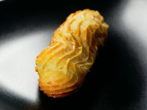 One eclair on a black background. Choux pastry. Foto stock