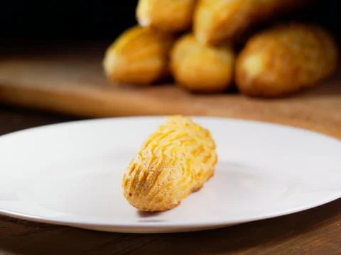 One eclair on a white plate, on a dark wooden background. Homemade baking. Stock Photos