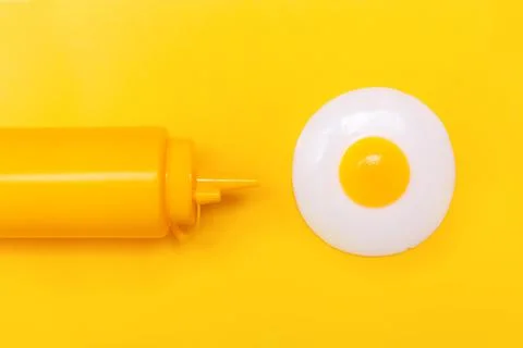 One egg fried with mustard in a plastic bottle on a yellow background. Idea f Stock Photos