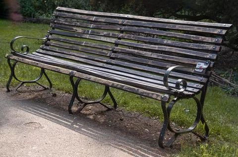 One empty bench made of old wooden boards and black iron stands in the park. Stock Photos