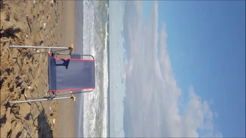 One empty blue folding touring chair on ocean shore. Large sea waves, white foam Stock Footage 144110972