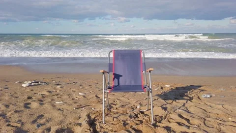 One empty blue folding touring chair on ocean shore. Large sea waves, white foam Stock Footage 144110986