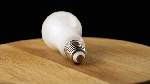 One Energy Saving Light Bulbs Spinning on a Wooden Board, Black Background Video stock 246120020