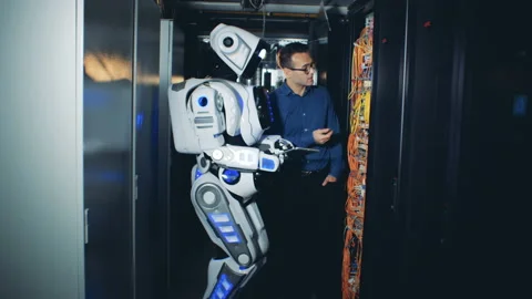 One engineer and a cyborg stand in a special room, checking server equipment. 4K Stock Footage 98585147