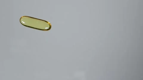 One fish oil capsule is rolled over a transparent surface playing with medicine Stock Footage 267420936