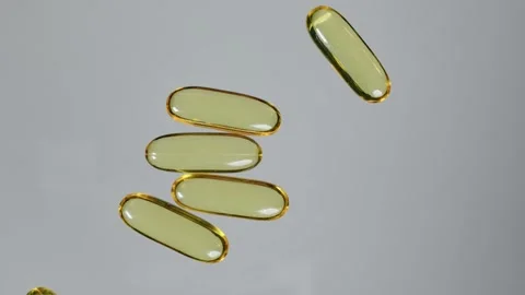 One fish oil capsule is rolled toward a pile of capsules with vitamin E or fish Stock Footage 267420941