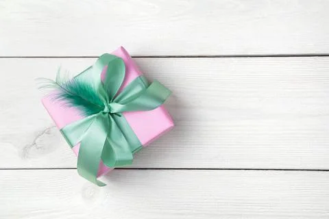 One gift box decorated with a mint-colored ribbon and feather on a white wooden Stock Photos