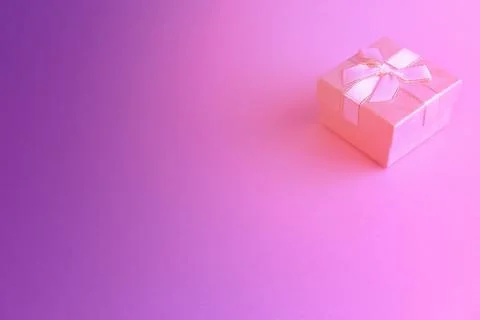One gift or present box with a white ribbon bow on a pink and purple trend ba Stock Photos