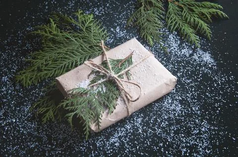 One gift is wrapped in kraft paper with fir sprigs on a black board. Stock Photos