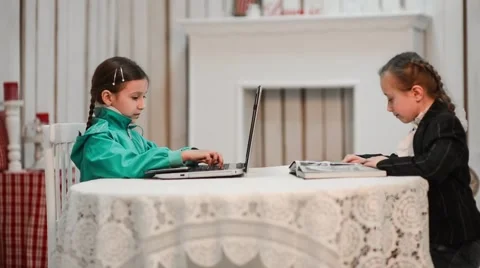 One girl is sitting at the computer the second reading a book Stock Footage 48376269