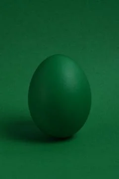 One green painted Easter egg stand on a green background. 스톡 사진