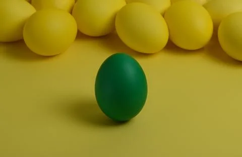 One green painted Easter egg stands in front of yellow eggs Stock Photos