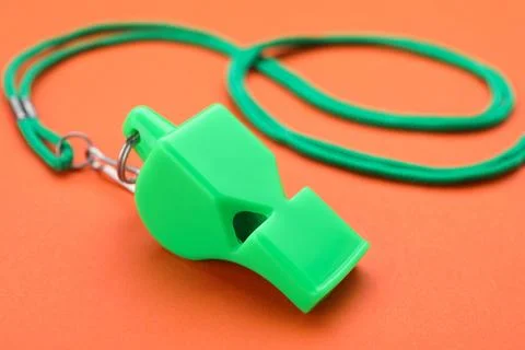 One green whistle with cord on orange background, closeup Stock Photos