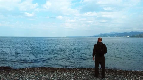 One guy with a beard in a gray suit stands on the shore of a calm sea Stock Footage 220645001