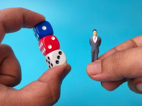 One hand pinches a stack of blue, red, and white dice while another hand ho.. 库存照片