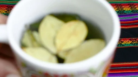 One hand show a cup of a Coca leaves tea in front of the camera Stock Footage