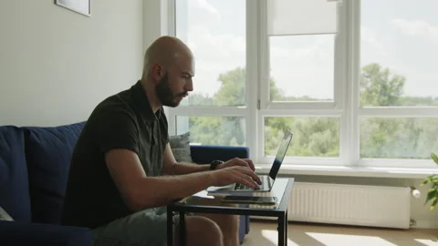 One handsome bearded man working on laptop at home, stops to think, looking into Stock Footage 166527964