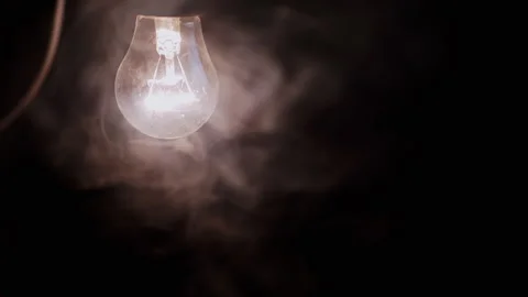 One Hanging, Glowing Light Bulb with a Wire in Thick Smoke on a Black Background Stock Footage 253772111