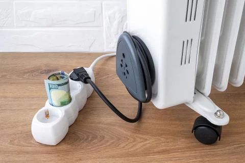 One hundred dollar bill inserted into extension cord near oil heater plug. Stock Photos