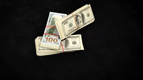 One hundred dollar bundles fall in a pile on a table in slow motion. Stock Footage 129786332