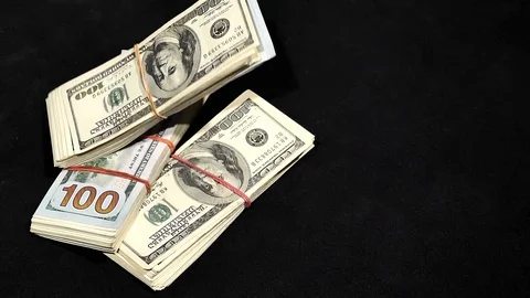 One hundred dollar bundles of notes fall on the table in slow motion. Video stock 129786464