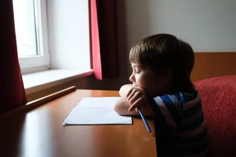 One kid sits at the table and looks at copybook and reads a task. The child.. Stock Photos