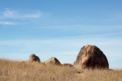 One large boulder and three smaller big rocks set against blue sky with white Stock Photos