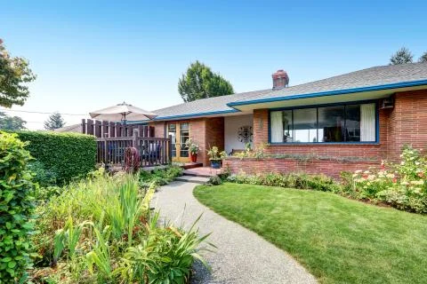 One level Red brick rambler house exterior with concrete walkway and trimmed  Stock Photos