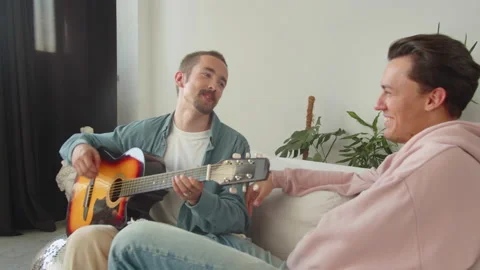 One of lgbt men is making laugh his boyfriend by playing guitar impulsively Stock Footage 174453614