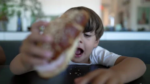 One little boy grabbing bread taking a bite of carb food seated at table Stock Footage 221232293