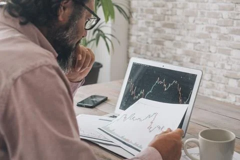 One man looking and studying stock market charts at the desk with opened lapt Stock Photos