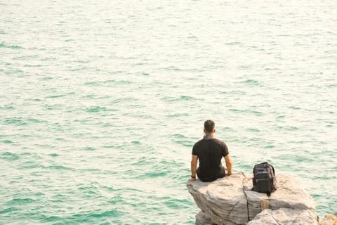 One man sit in back on rock by the sea with backpack. 스톡 사진
