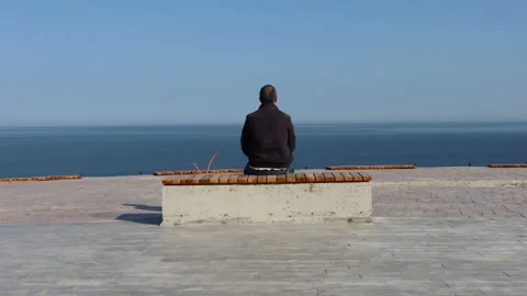 One man sits alone in front of the sea view. Man sitting on the bench by the sea Vídeos de archivo 153052469