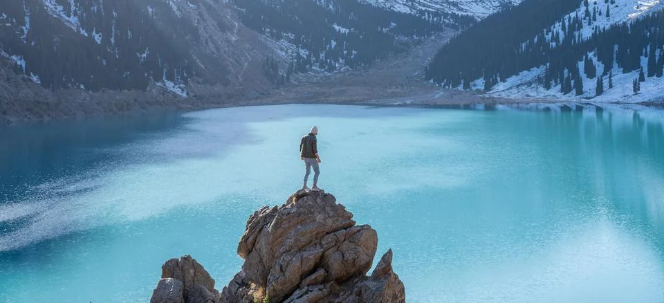 One man standing on a boulder on a vantage point over mountain lake Stock Photos