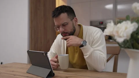 One man use digital tablet have video call online and hold cup at home Stock Footage 276477496